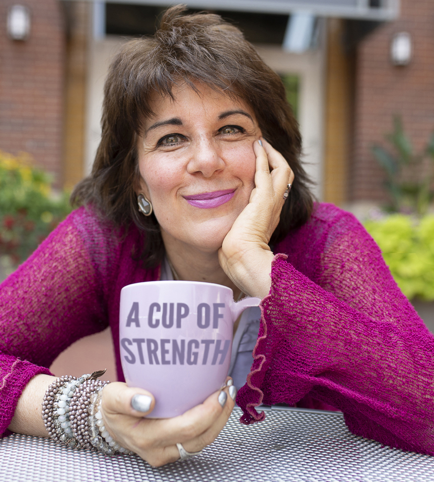 Picture of Tama Kieves smiling at the camera holding a cup that says "A Cup of Strength"